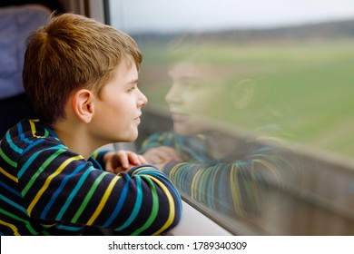 Adorable Kid Boy Traveling By Train. Happy Smiling Child Looking Out Of The Window During Train Moving. Kid Dreaming And Wondering. Family Vacations And Journey Trip.