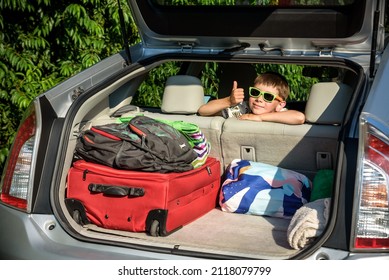 Adorable Kid Boy Wearing Sunglasses Sitting In Car Trunk. Portrait Of Happy Child With Open Car Boot While Waiting For Parent Get Ready For Vocation. Family Trip Traveling By Car Concept.