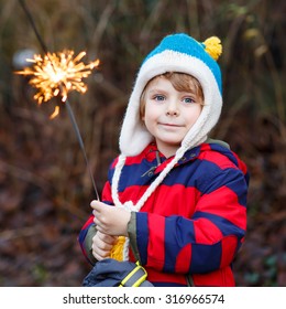 Adorable Kid Boy In Winter Clothes Holding Burning Sparkler On New Year's Eve. Safe Fireworks For Kids Concept. Happy Child Having Fun Outdoors.