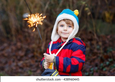 Adorable Kid Boy In Winter Clothes Holding Burning Sparkler On New Year's Eve. Safe Fireworks For Kids Concept. Happy Child Having Fun Outdoors.