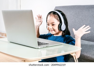 An Adorable Kid Girl Happy Online Studies With A Laptop And Headphones Set At Home Due To The Covid-19 Coronavirus Pandemic. Online Education Learning Gaming Technology And Homeschooling Concept Idea.