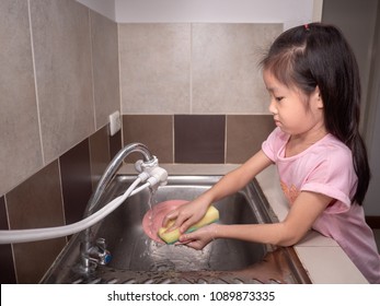 Adorable  Kid Girl Washing Dishes In Domestic Kitchen. Child Having Fun With Helping His Parents With Housework.