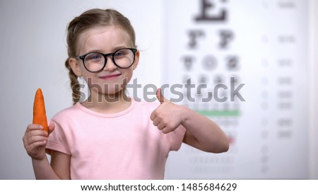 Adorable kid in glasses showing thumbs up to carrot, beta-carotene for eyes