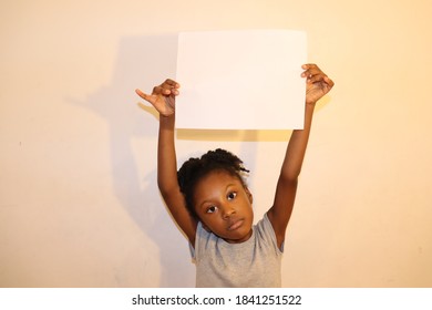 Adorable Kid With Serious Face Expression Holding Blank Paper Sign Above Head White Background Inddors