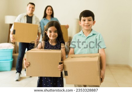 Adorable kids carrying cardboard boxes and helping mom and dad to unpack while moving into a new house or apartment