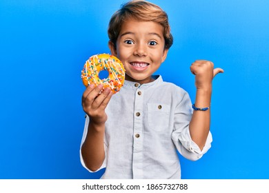 Adorable Latin Kid Holding Donut Pointing Thumb Up To The Side Smiling Happy With Open Mouth 