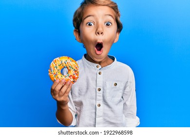 Adorable Latin Kid Holding Donut Scared And Amazed With Open Mouth For Surprise, Disbelief Face 