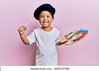 Adorable latin toddler smiling happy wearing artist style using paintbrush and palette over isolated pink background. - Powered by Shutterstock