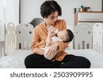 Adorable little Asian baby sleep during drinking milk from baby bottle. Asian mother holding adorable her son and feeding milk from milk bottle. Concept babies healthcare.