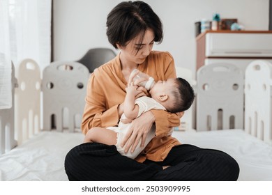 Adorable little Asian baby sleep during drinking milk from baby bottle. Asian mother holding adorable her son and feeding milk from milk bottle. Concept babies healthcare. - Powered by Shutterstock