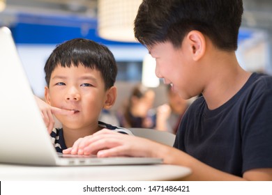 Adorable Little Asian Boy Thinking And Studying Online Lessons With Happy Preteen Brother From Laptop Computer. Brotherhood, Kids, E-learning, Gamification, Coding, Social Media, Online Education.