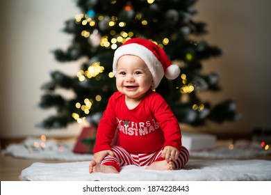 adorable little baby boy in a red christmas outfit sitting on a soft fake fur in front of a christmas tree - Shutterstock ID 1874228443