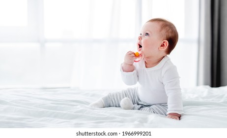 Adorable little baby boy sitting in the bed and holding dummy in his hand close to his mouth. Beautiful toddler child in the bedroom in the morning time. Cute kid alone at home - Shutterstock ID 1966999201