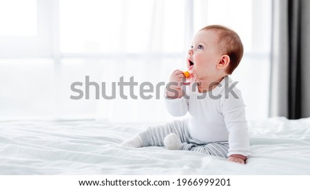 Adorable little baby boy sitting in the bed and holding dummy in his hand close to his mouth. Beautiful toddler child in the bedroom in the morning time. Cute kid alone at home