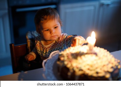 Adorable little baby girl celebrating first birthday. Child blowing one candle on homemade baked cake, indoor.