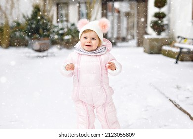 Adorable little baby girl making first steps outdoors in winter. Cute toddler learning walking. Child having fun on cold snow day. Wearing warm baby pink clothes and hat with bobbles