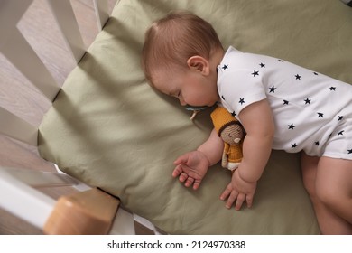 Adorable little baby with pacifier and toy sleeping in crib, above view