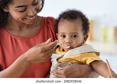 Adorable Little Black Baby Boy Eating From Spoon, Closeup Shot Of Caring African American Mother Feeding Her Cute Infant Son With Mash Fruit Puree Or Porridge, Giving Healthy Food To Toddler Child