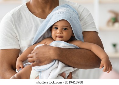 Adorable Little Black Infant Baby Wrapped In Blue Towel Relaxing In Father's Arms After Bath, Cute African American Toddler Child Looking At Camera, Enjoying Daddy's Care, Cropped Shot, Closeup