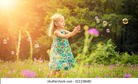 Adorable little blond girl having fun playing with soap bubbles during sunny summer afternoon