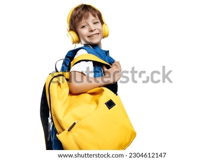 Adorable little boy wearing headphone and yellow backpack looking to camera on white background. Back to School