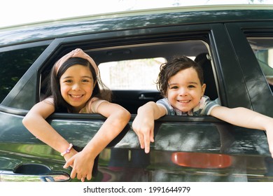 Adorable little brother and sister smiling and making eye contact while putting their heads in the car window. Excited siblings waiting for their parents for a family trip