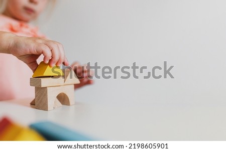 Adorable little child girl of preschooler age playing wooden building blocks at home or kindergarten. Toddler kid is stacking a tower from colourful cube toys on the table. Kids Play Room. Banner size