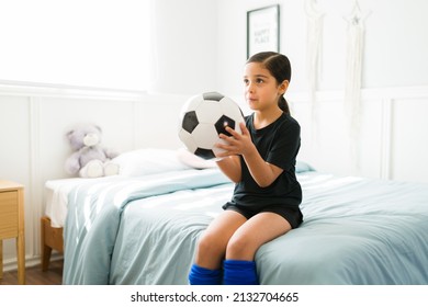 Adorable Little Child Holding A Ball While Sitting On Her Bed And Ready To Go To A Football Soccer Practice 