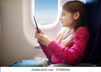 Adorable little child traveling by an airplane. Girl sitting by aircraft window and reading her ebook during the flight. Traveling abroad with kids.