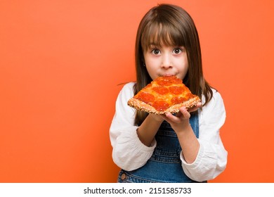 Adorable little girl biting a slice of pizza and enjoying her food in a studio with copy space - Powered by Shutterstock