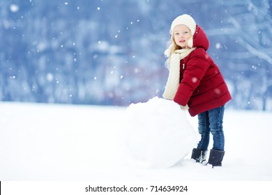 Adorable Little Girl Building A Snowman In Beautiful Winter Park. Cute Child Playing In A Snow. Winter Activities For Kids.