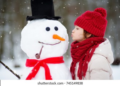 Adorable Little Girl Building A Snowman In Beautiful Winter Park. Cute Child Playing In A Snow. Winter Activities For Kids.