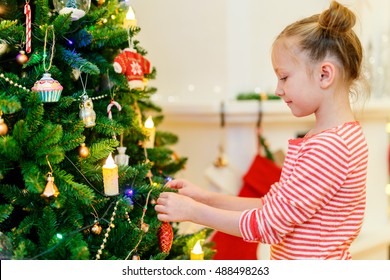 Adorable Little Girl Decorating Christmas Tree With Colorful Glass Baubles At Home