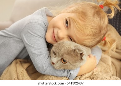 Adorable kleine Mädchen, die süße Katze auf dem Sofa umarmen, Nahaufnahme
