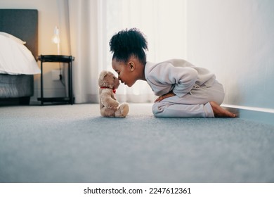 Adorable little girl enjoying her childhood at home with her favourite toy, a cute teddy bear. She touches noses with the stuffed animal, enjoying her leisure time and the innocence of childhood.
