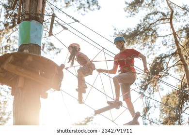 Adorable little girl enjoying her time in a rope playground structure at adventure park, her father supporting her, family weekend activities. - Powered by Shutterstock