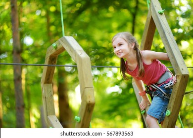 Adorable Little Girl Enjoying Her Time In Climbing Adventure Park On Warm And Sunny Summer Day. Summer Activities For Young Kids. Child Having Fun On School Vacations. 