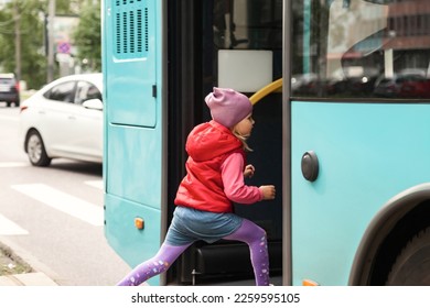 Adorable little girl enters to bus of public modern transport outdoors. Cute child in metropolitan transport, rides on vehicle. Concept of public transport and urban lifestyle. Copy text space