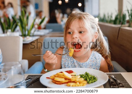 Adorable little girl having breakfast at resort restaurant. Happy preschool child eating healthy food, vegetables and eggs in the morning.