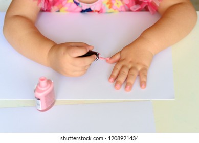 Adorable Little Girl Having Fun Playing At Home With Colorful Pink Nail Polish Doing Manicure And Painting Nails. Toddler Cute  Child In Pink Elegant Dress Sitting Wood White Table And Making Manicure