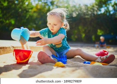 Adorable Little Girl Having Fun On Playground In Sandpit. Toddler Playing With Sand Molds And Making Mudpies. Outdoor Creative Activities For Kids