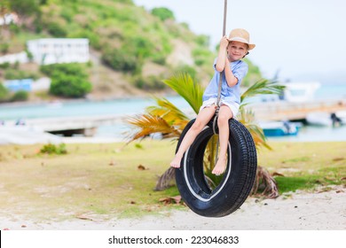Adorable little girl having fun on tire swing on summer day