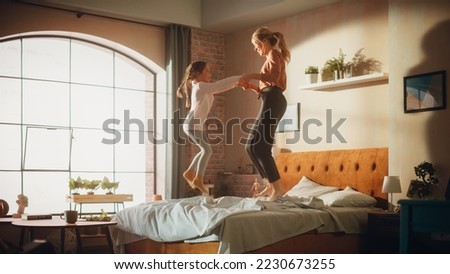 Adorable Little Girl Having Fun at Home with Young Beautiful Mother. Family Playing at Home, Cheerfully Jumping and Falling onto a Bed in Stylish Loft Apartment with Big Window. Happy Childhood.