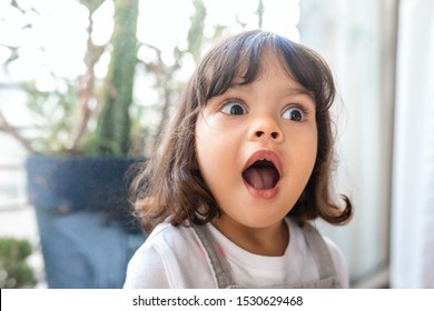 Adorable Little Girl With Her Mouth And Eyes Wide Open In Surprise While Playing In Her Living Room At Home