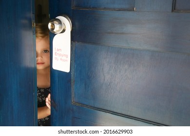 Adorable Little Girl In Hotel Room Opening The Door With Enjoying My Room Tag Hanging On Door Handle. Family Vacation Concept. 