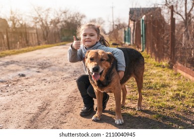 Adorable little girl hugging a large brown yard dog on a village street.
