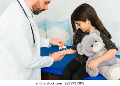 Adorable little girl hugging a teddy bear getting a skin prick test for her allergies with a pediatrician doctor - Powered by Shutterstock