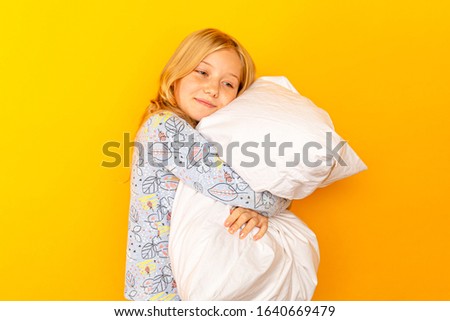 Adorable little girl looking at the camera and hugging a pillow background of a yellow wall