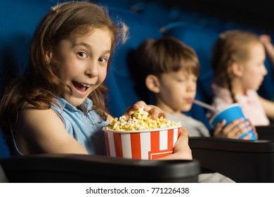 Adorable little girl looking excitedly to the camera enjoying movie premiere at the local cinema holding big popcorn bucket copyspace lifestyle entertainment activity leisure spectator concept - Shutterstock ID 771226438