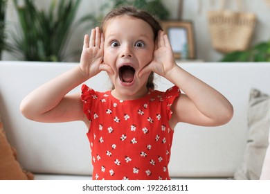 Adorable little girl making faces while sitting on sofa ta living room - Powered by Shutterstock